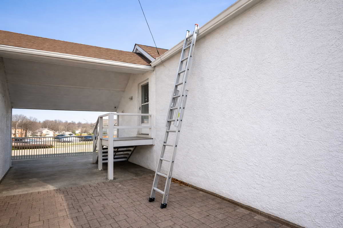An extension ladder positioned against a home's exterior for gutter and upper-wall maintenance work
