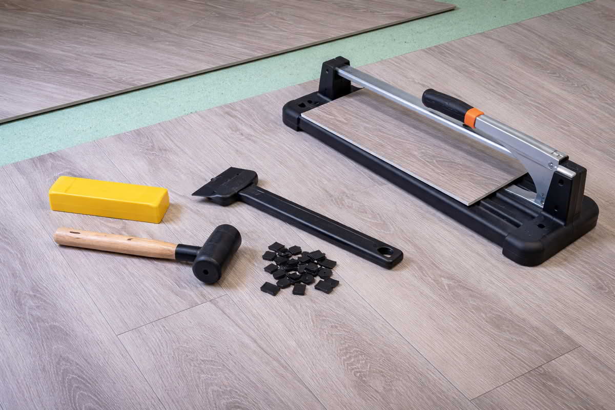 Laminate and vinyl flooring tools including tapping block, pull bar, spacers, and cutter arranged beside plank flooring