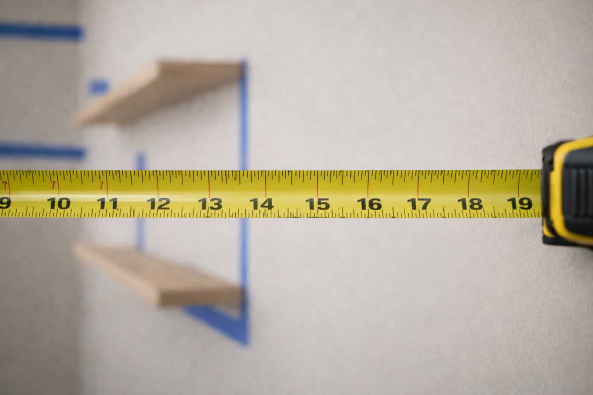 A tape measure extended across a wall during a home shelving layout project with clear markings visible on the blade